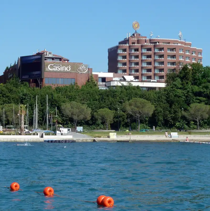 A Grand Casinò Portorož épülete a feliratával a tenger felől nézve, mellette a Hotel Metropol tornya