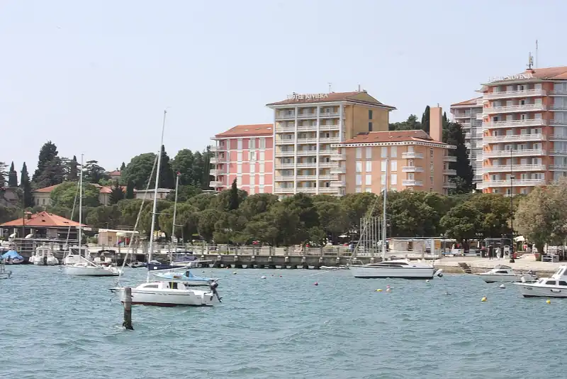 A portoroži tengerpart az öböl felől, a fenyők mögött a Hotel Riviera és a Hotel Slovenija